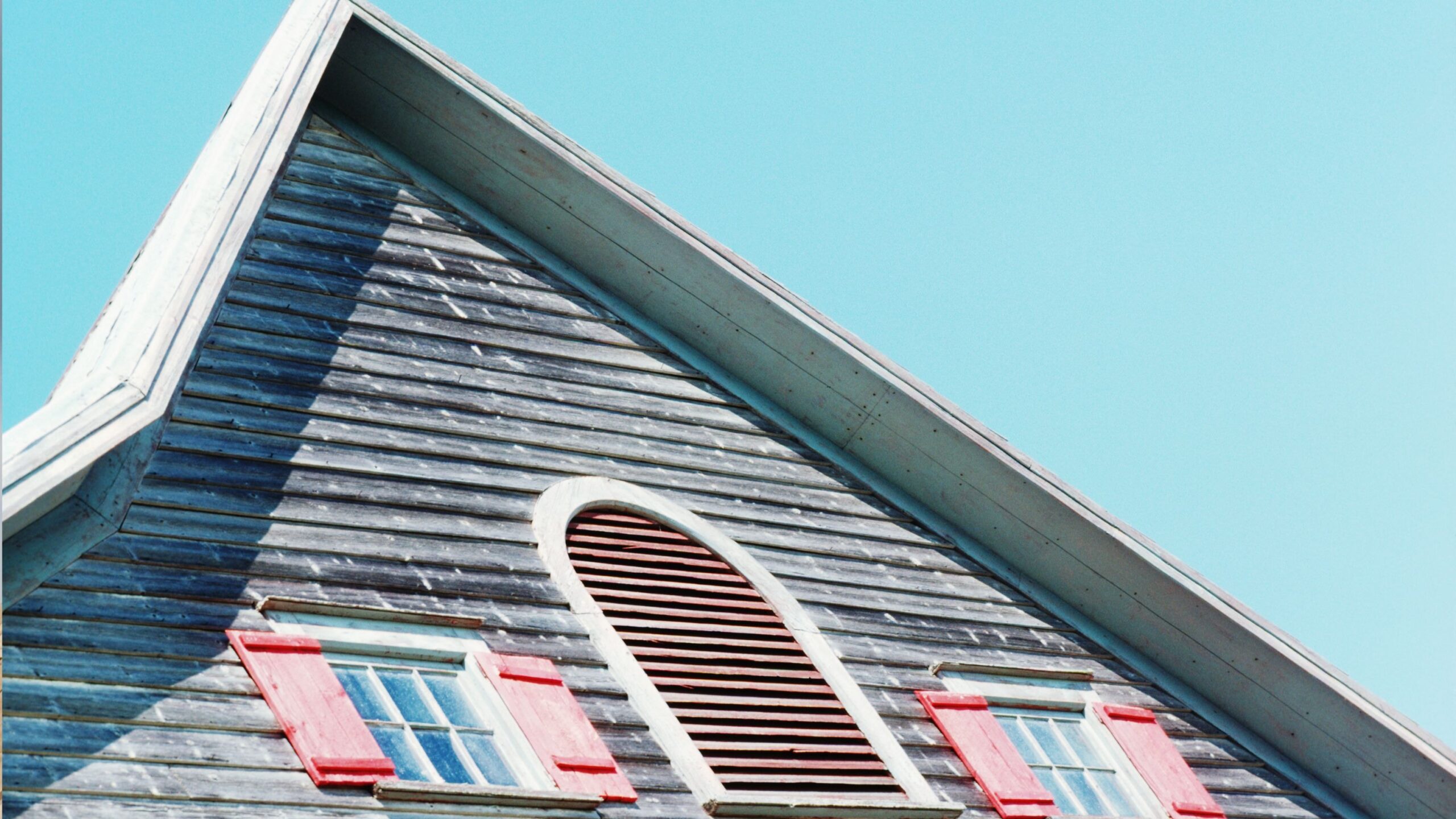 Classic wooden house with red shutters and steep roof under bright sky