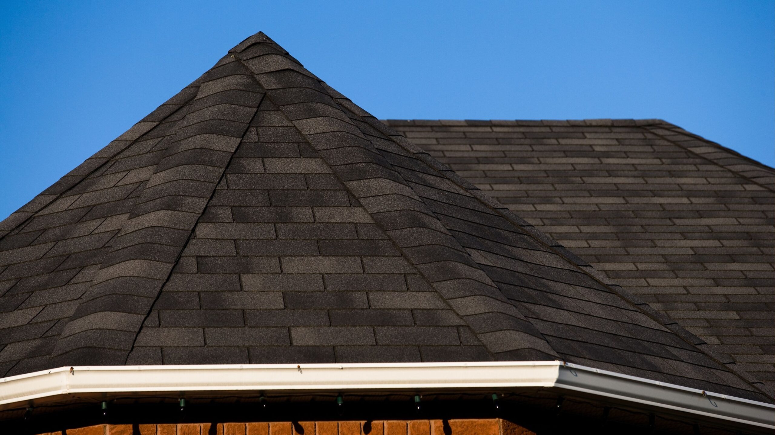 Dark shingle roof on a house with brick siding and a visible gutter system