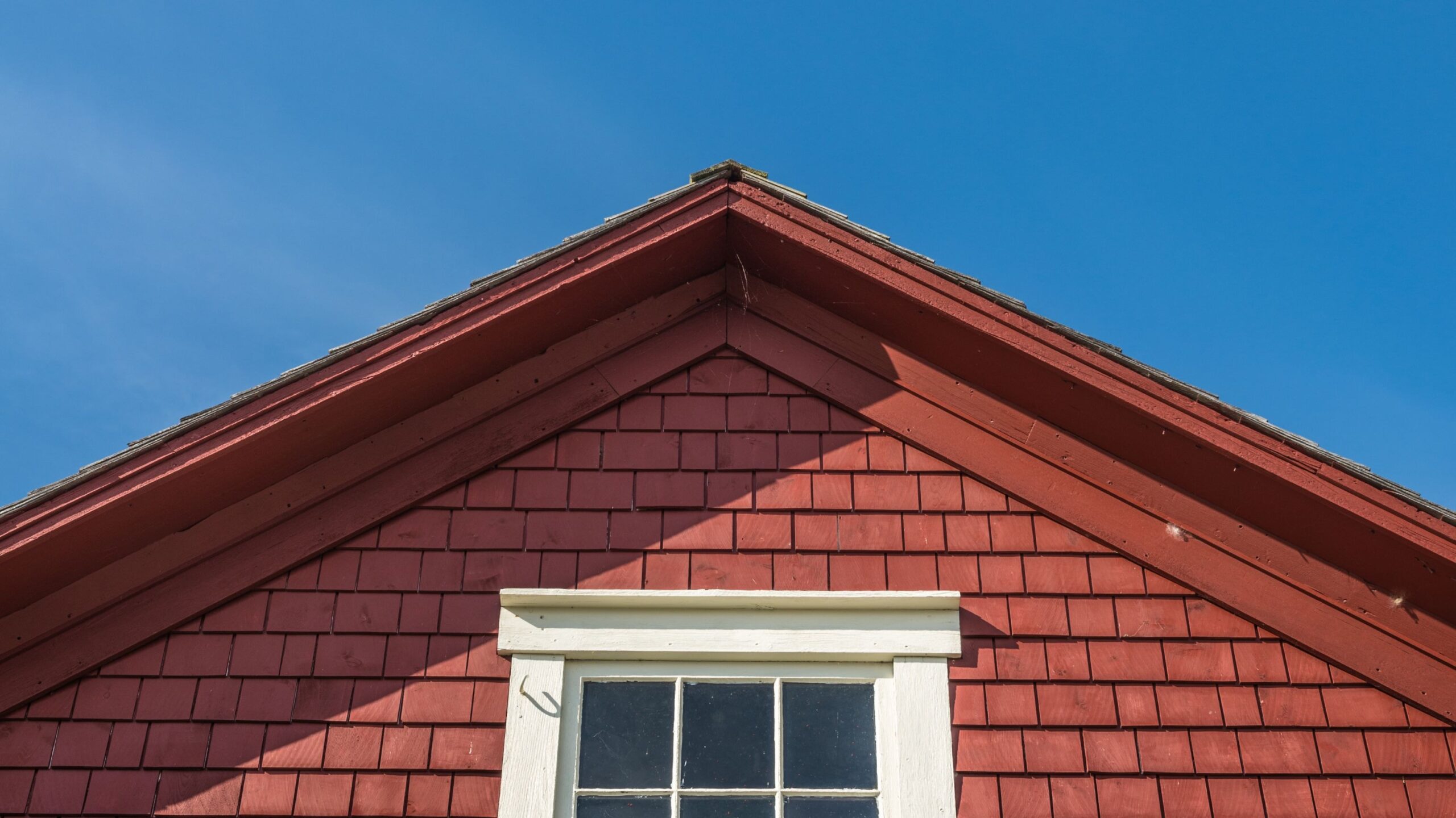 Red-shingled roof on a traditional wooden house under a clear blue sky