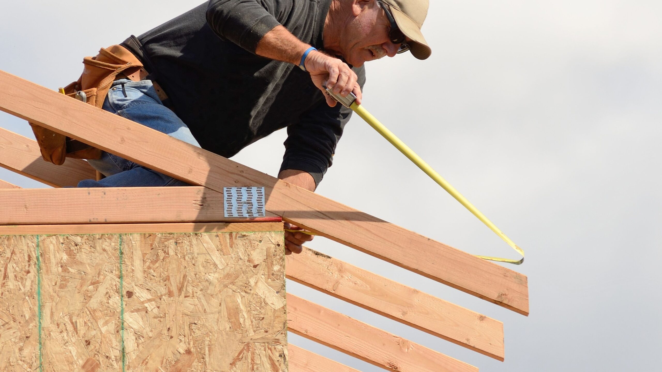 Worker measuring rafter length with a tape measure on a roof frame